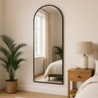 Full-length mirror leaning against a wall in a bedroom with a plant and nightstand.
