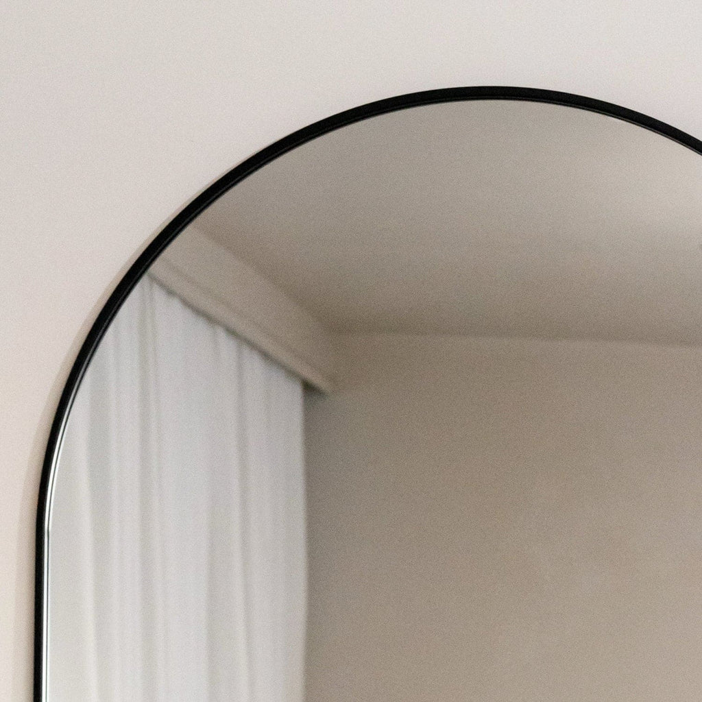 Round mirror with black frame on a white wall