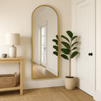 Full-length mirror with gold frame in a room with a lamp, plant, and wooden shelf.