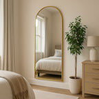 Gold-framed mirror in a bedroom with a bed, plant, and nightstand.