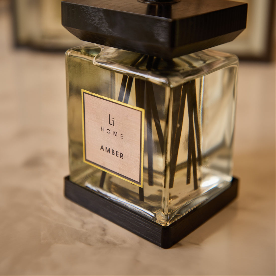 Glass diffuser with wooden top labeled 'Li Home Amber' on a neutral background