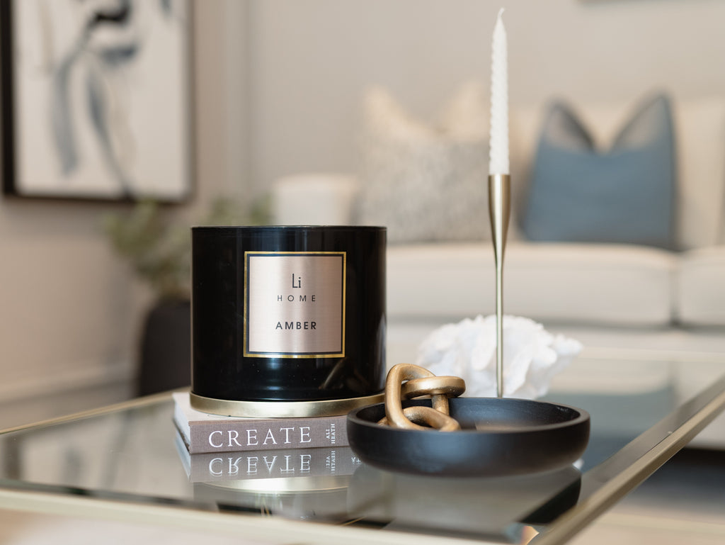 Black candle labeled 'LI Home Amber' on a coffee table with a blurred living room background