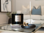 Black candle labeled 'LI Home Amber' on a coffee table with a blurred living room background