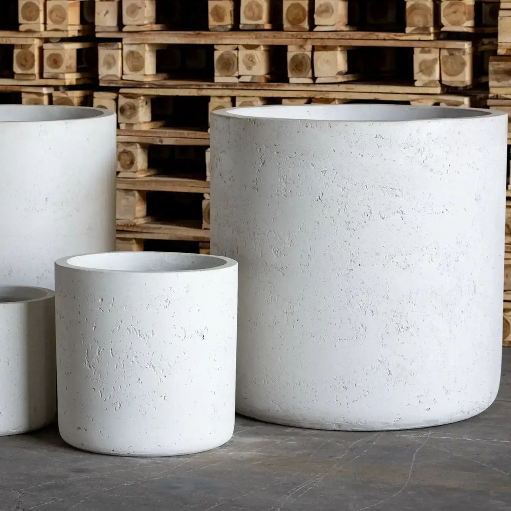 Three concrete planters of different sizes in front of wooden pallets.