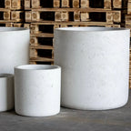 Three concrete planters of different sizes in front of wooden pallets.