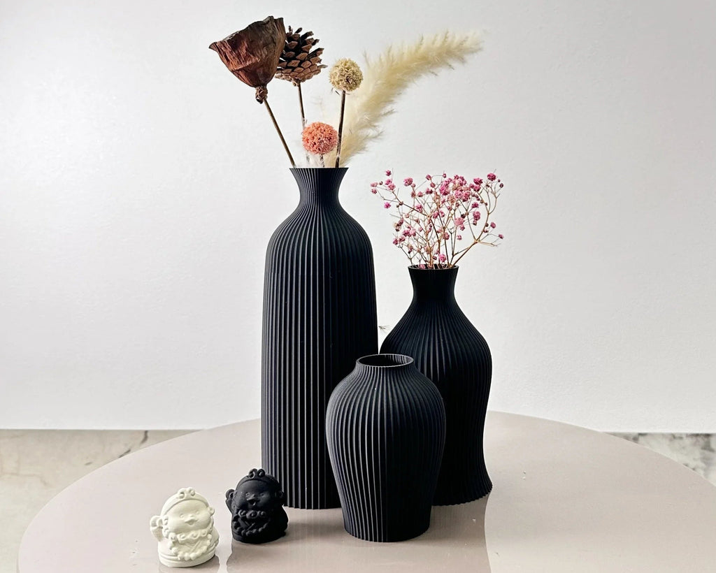 Set of black textured vases with decorative elements on a light surface.
