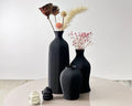 Set of black textured vases with decorative elements on a light surface.