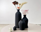 Set of black textured vases with decorative elements on a light surface.