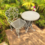 White metal garden chair and table set in a garden setting with greenery.