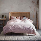 Two people lying in bed under a pink duvet in a bedroom setting.