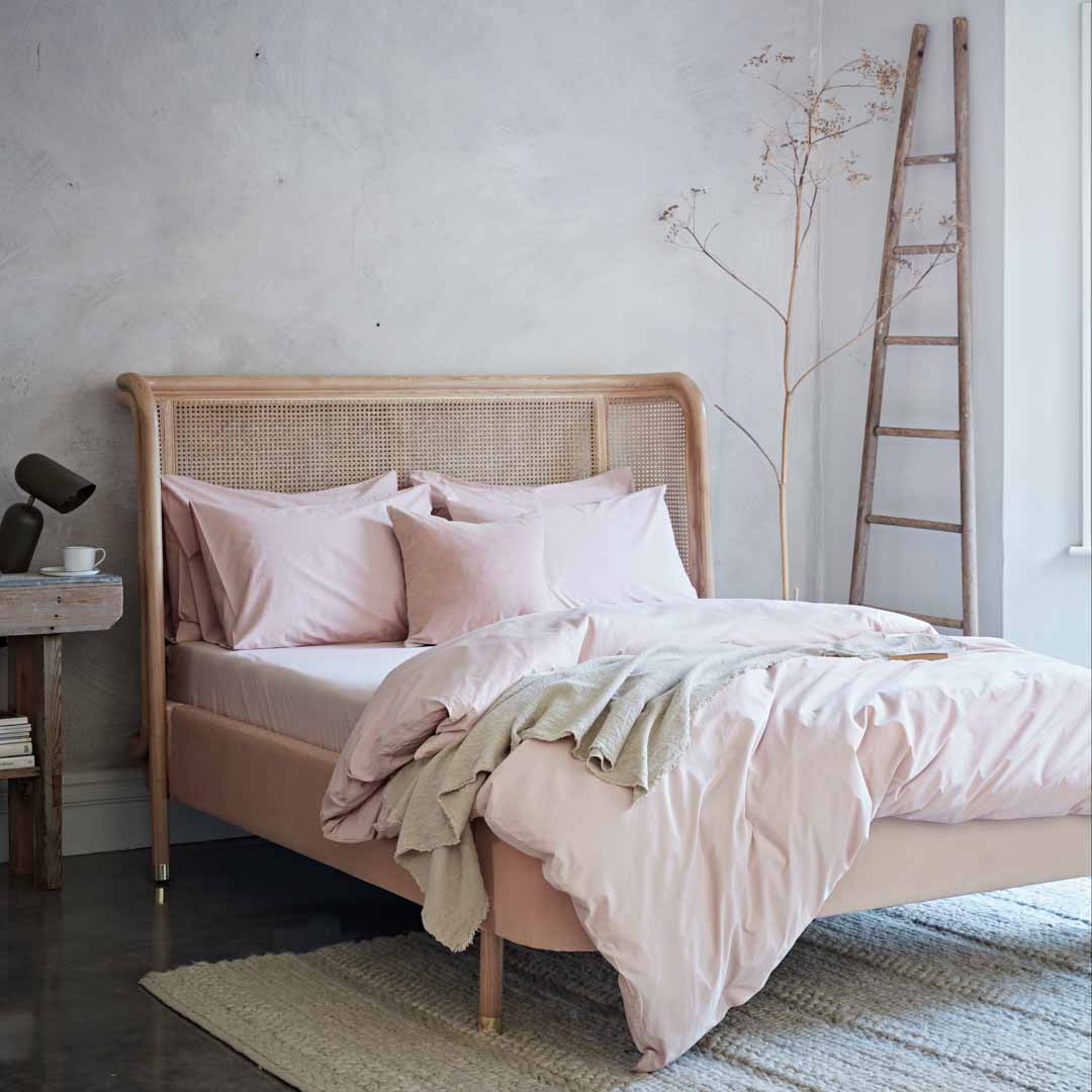 Bed with pink bedding and wooden headboard in a room with a ladder and small table.