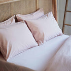 Set of white pillows on a bed with a wicker headboard.