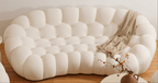 White tufted sofa with a blanket draped over it on a wooden floor.