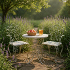 White metal garden table and chairs with a glass of juice and apples in a basket, set against a garden backdrop.