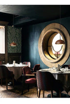 Dining area with round wooden mirror on the wall, tables, and chairs.