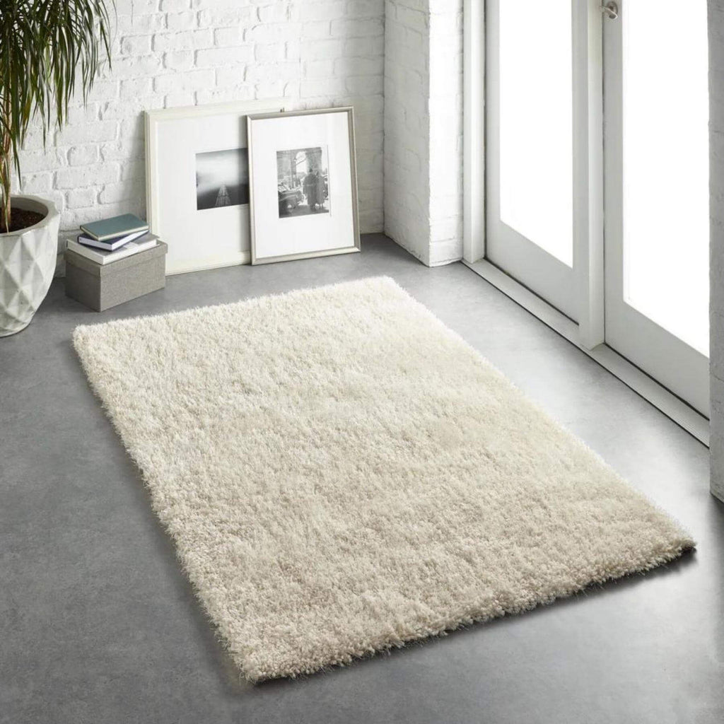 Beige rug on a gray floor with a white brick wall and framed pictures in the background.