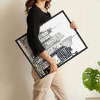 Person holding a framed black and white architectural drawing against a neutral background