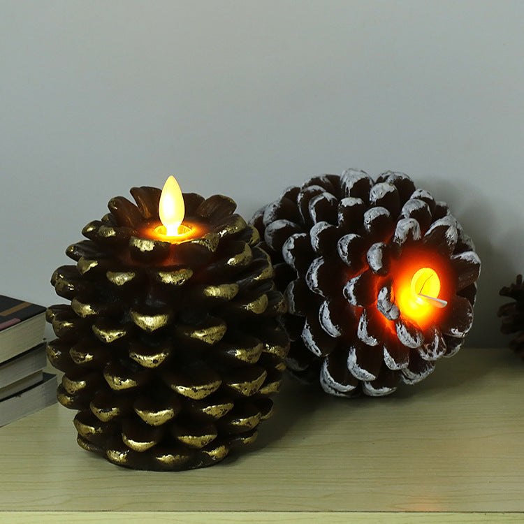 Two pine cone-shaped candles with glowing flames on a wooden surface.