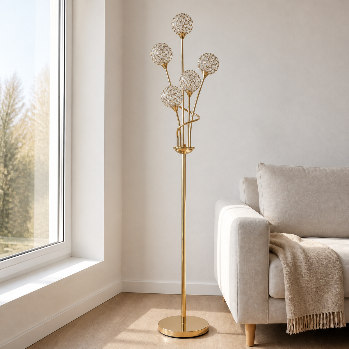 A modern gold floor lamp with five spherical crystal-like shades on branching stems, standing in a bright living room next to a light beige sofa and window.