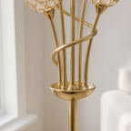 Close-up of a polished gold floor lamp with multiple slender stems, a spiral accent, a round base, and clear crystal-like globe shades in a softly lit interior setting.