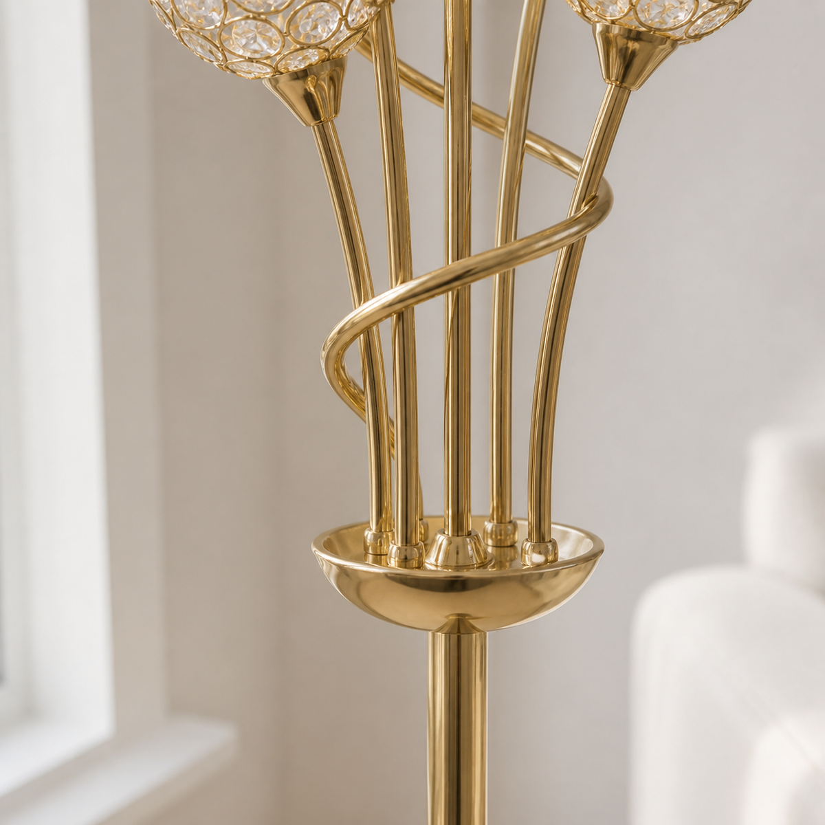 Close-up of a polished gold floor lamp with multiple slender stems, a spiral accent, a round base, and clear crystal-like globe shades in a softly lit interior setting.