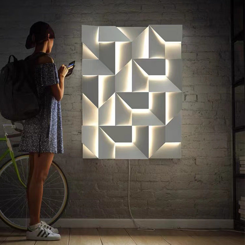 Woman using a phone next to a geometric wall art piece in a dimly lit room.