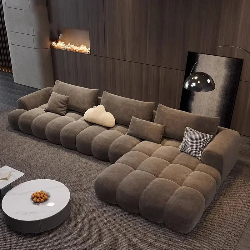 An L-shaped brown velvet sofa with multiple cushions, placed in a modern living room setting with a contemporary fireplace and decorative pillows.