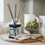A diffuser with black sticks on a wooden tray with a plant and other decor items.