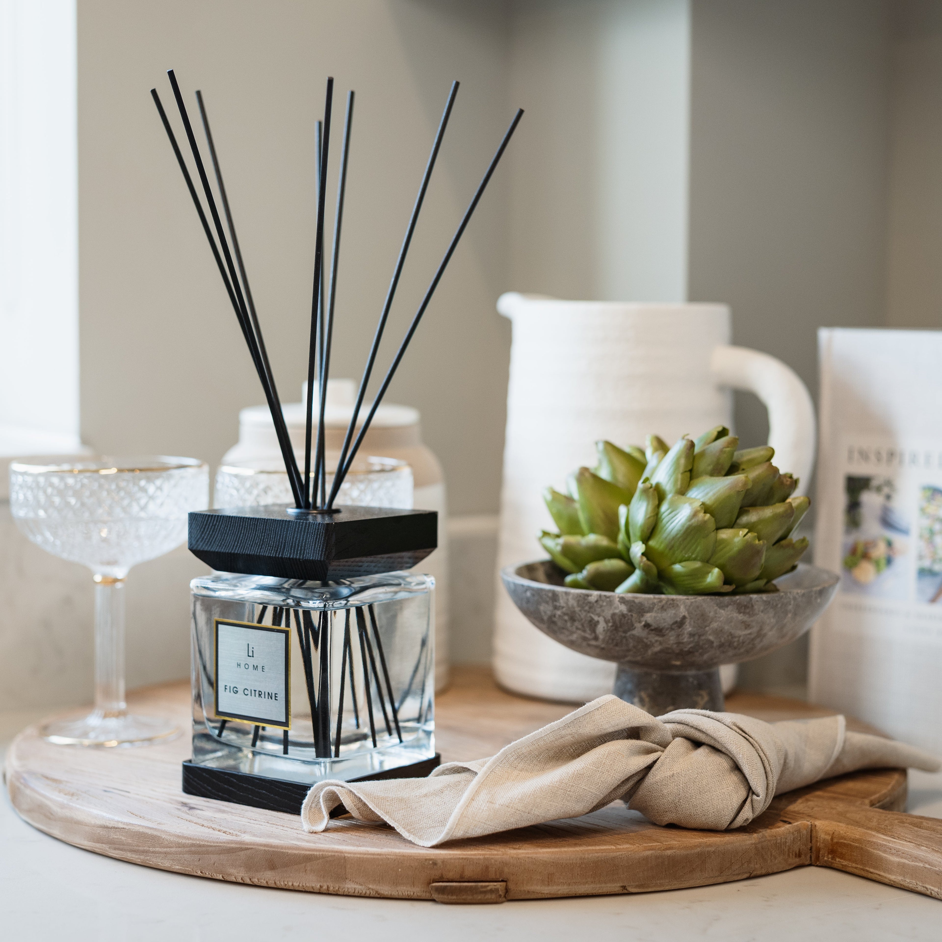 A diffuser with black sticks on a wooden tray with a plant and other decor items.