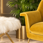 White faux fur ottoman with gold X-frame beside a mustard velvet armchair in a luxury interior