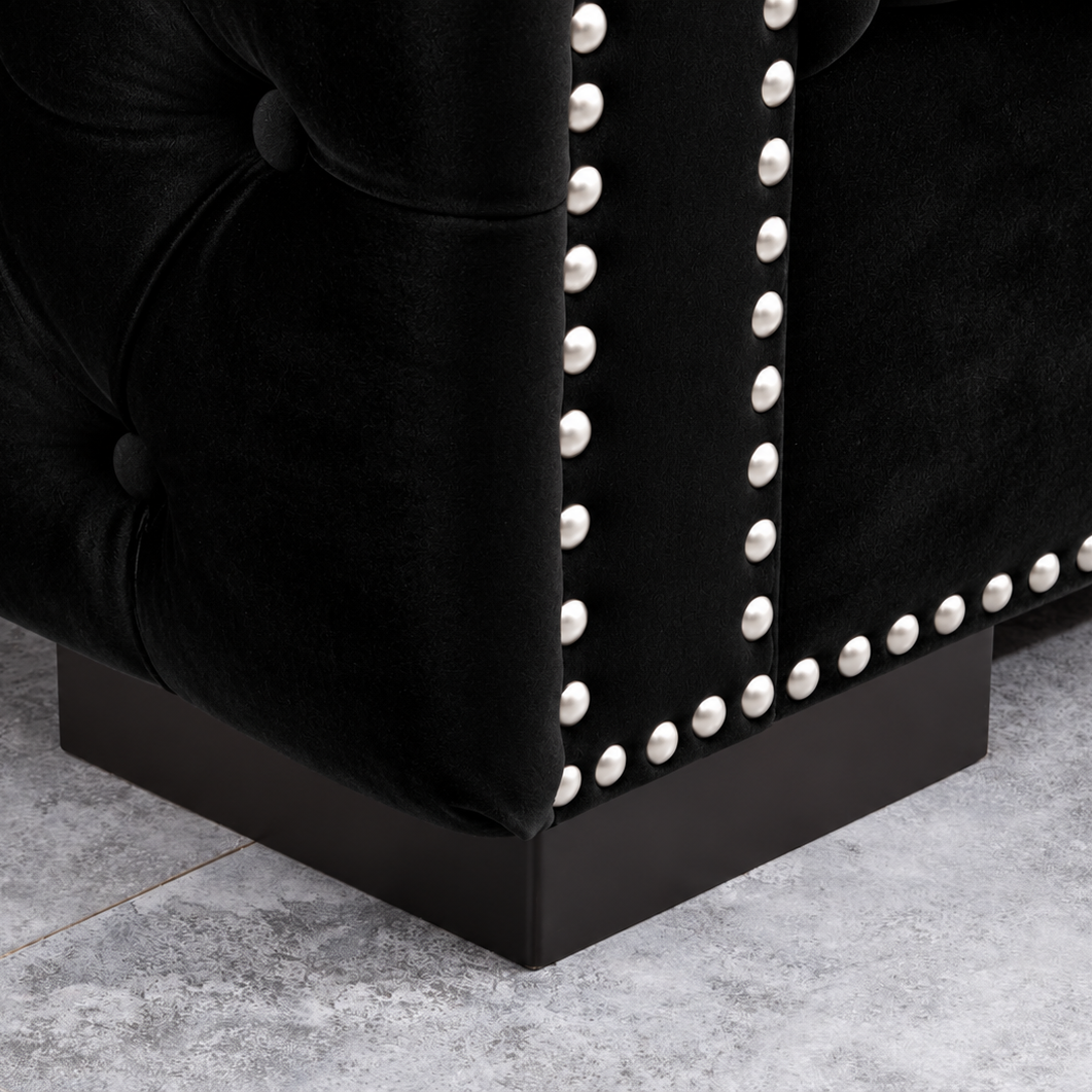 Close-up of a black tufted velvet upholstered furniture corner with silver nailhead trim and a dark wood base on a gray tiled floor.