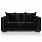 A black velvet loveseat sofa with matching throw pillows, featuring silver nailhead trim along the armrests and front edge, set against a clean white background with a subtle reflection below.
