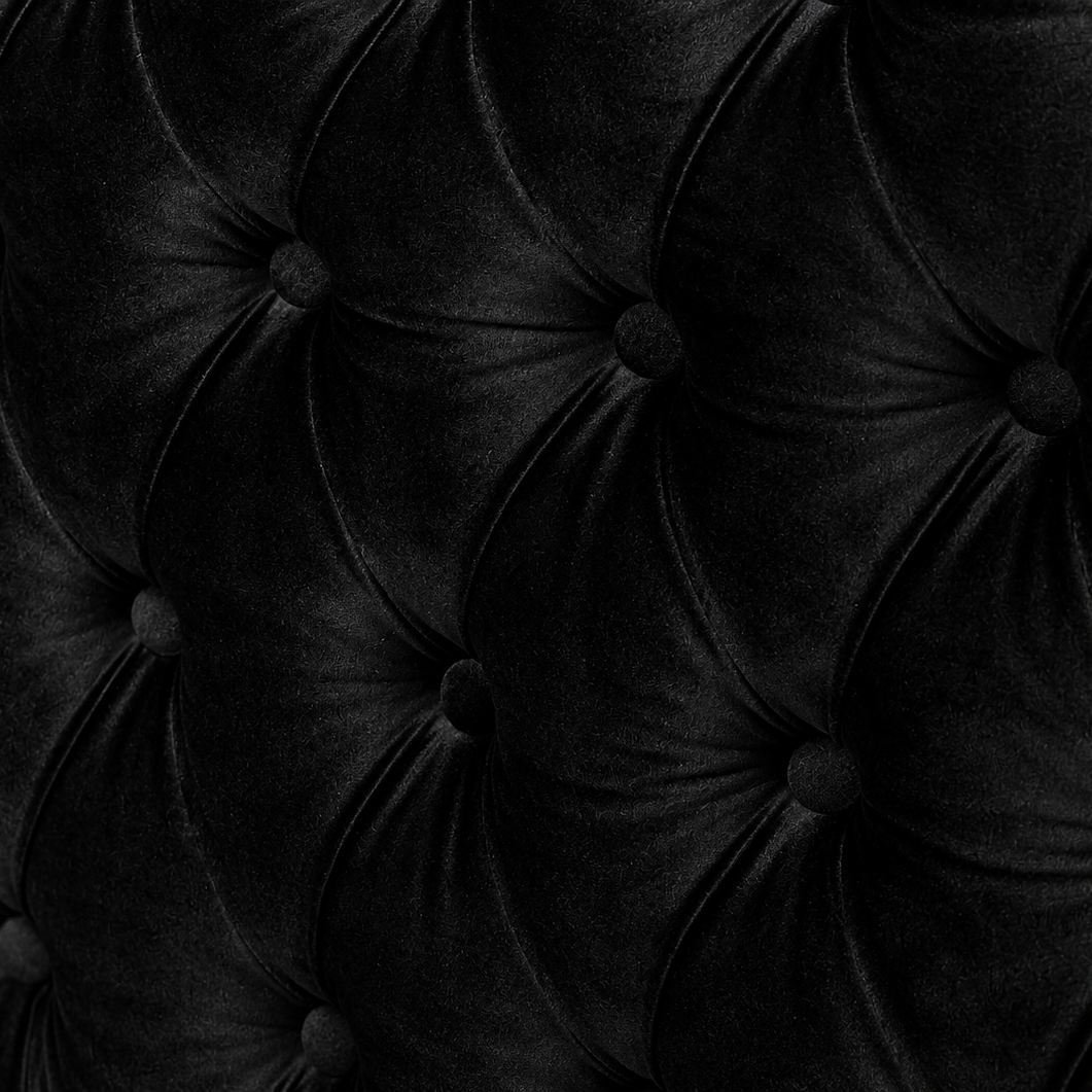 Close-up of a black tufted velvet upholstery surface with deep button tufting and a soft sheen.