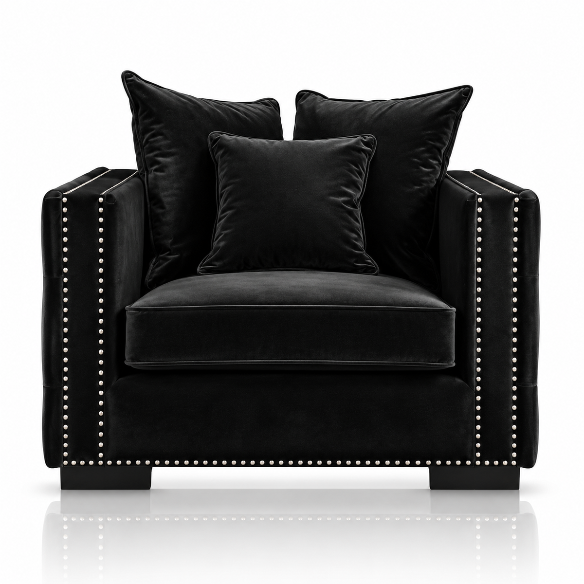 A black velvet armchair with matching throw pillows and nailhead trim, photographed on a clean white background with a subtle reflection below.