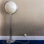 Floor lamp with a round white shade against a patterned wall.