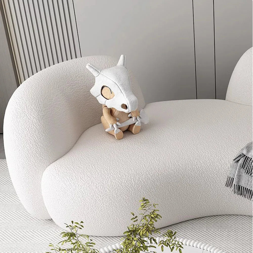 White plush toy with a unicorn design on a white cushion in a minimalistic room.