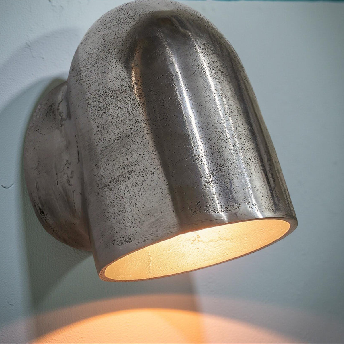 Metallic wall-mounted light fixture on a white wall with a blue background