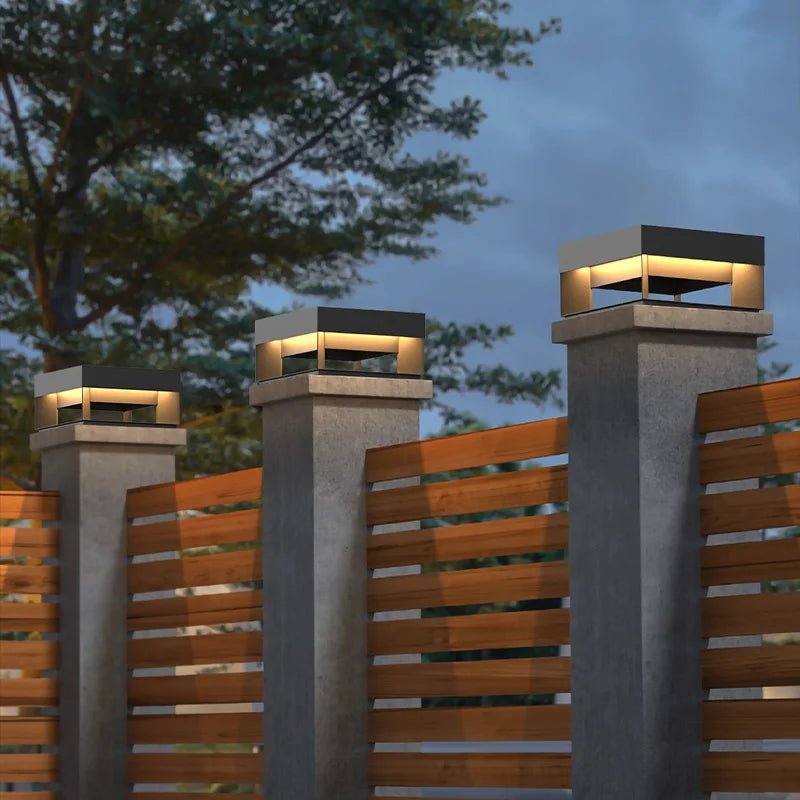 Decorative outdoor lights on concrete pillars with a wooden fence and trees in the background.