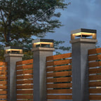 Decorative outdoor lights on concrete pillars with a wooden fence and trees in the background.
