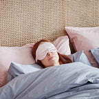 Person lying in bed with a sleep mask on, wearing pink pajamas.