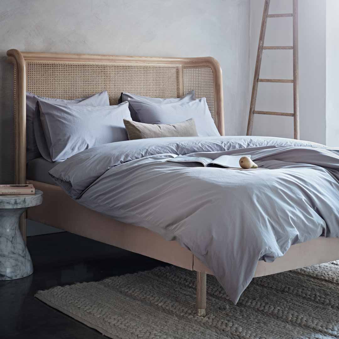 Neatly made bed with light gray bedding on a wooden bed frame in a bedroom setting.