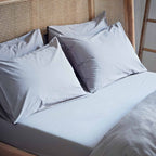 Light blue bedding set with pillows on a bed against a wooden headboard.