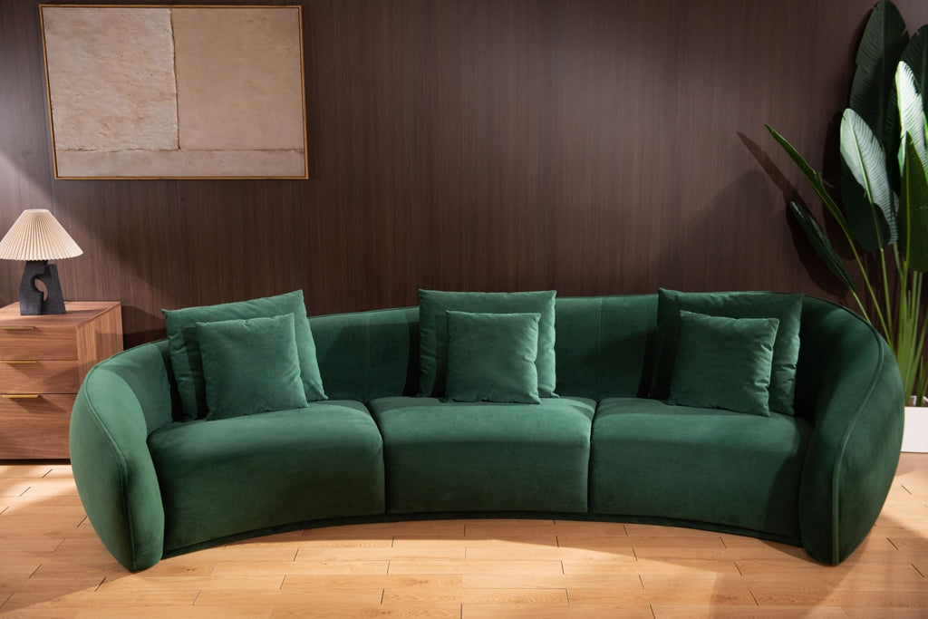 Green sectional sofa in a room with wooden flooring and a plant.