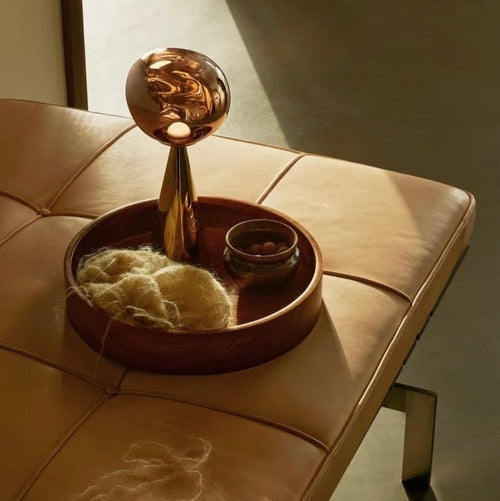 Decorative object with a metallic top and textured base on a beige cushioned surface.