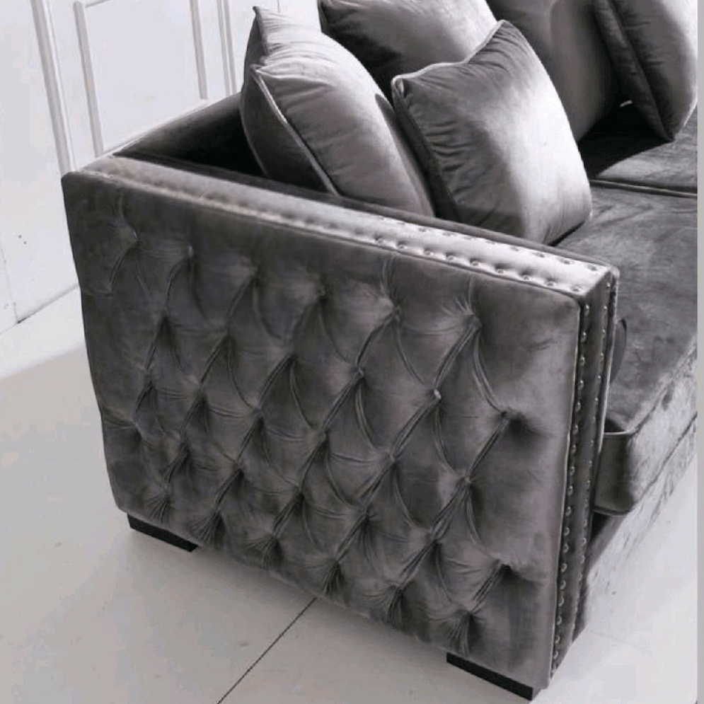 Gray tufted velvet ottoman with cushions on a white floor.
