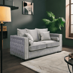 Gray tufted sofa in a living room setting with a lamp, rug, and plant.
