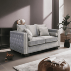 Gray tufted sofa in a modern living room with a plant and ottoman.