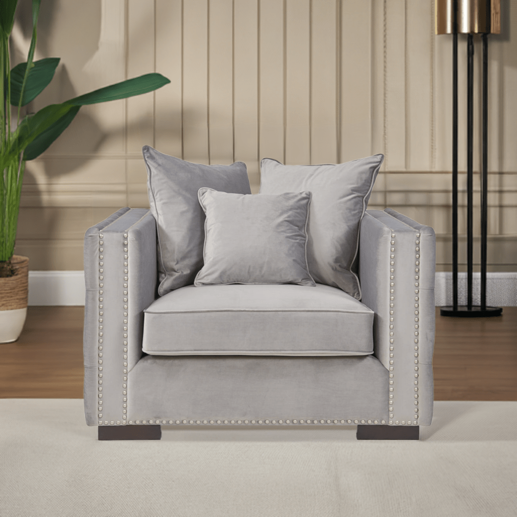 Gray armchair with decorative pillows in a room setting with a plant and lamp.