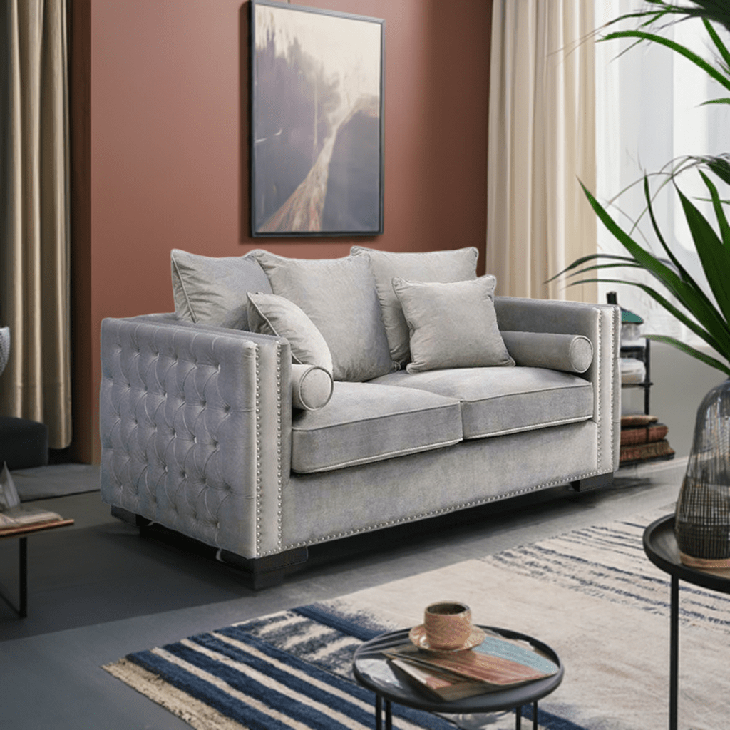 Gray tufted sofa in a living room with a rug, coffee table, and plant.