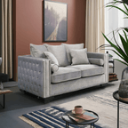 Gray tufted sofa in a living room with a rug, coffee table, and plant.
